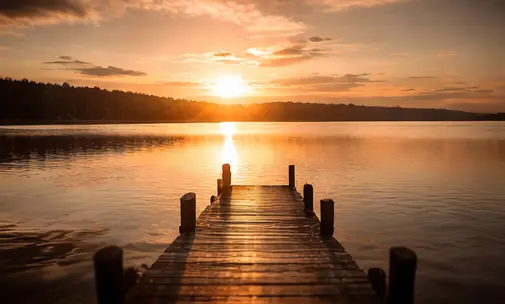 Un ponton en bois s'avançant sur un lac calme au coucher du soleil, symbolisant l'apaisement et le cheminement intérieur d'un récit de vie.